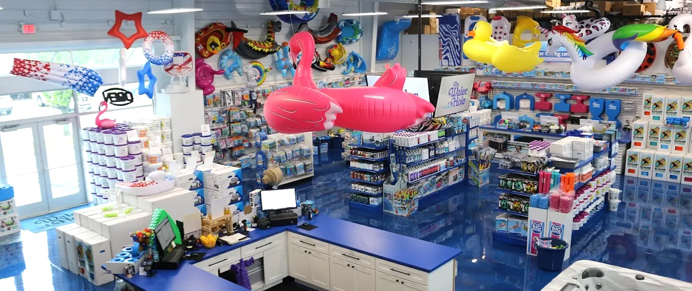 The Water Hole showroom displays pool supplies, hot tubs, and above-ground pool equipment with colorful inflatable decorations