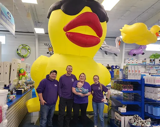 Family smiling with giant yellow duck mascot at The Water Hole pool supplies store