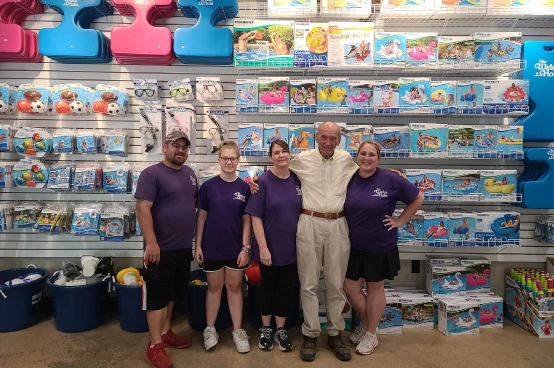 The Water Hole team and customer posing together in pool supplies showroom with shelving