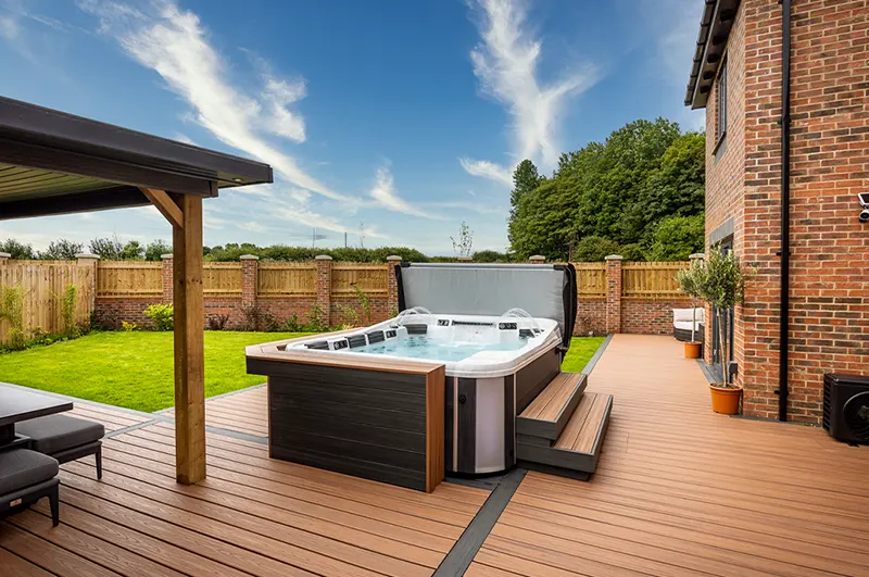 Modern luxury hot tub on composite deck with brick home and manicured backyard