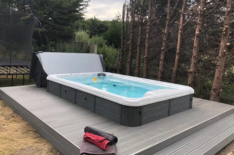 Modern above-ground pool with cover installed on residential deck surrounded by trees