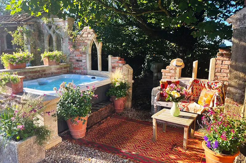 Backyard relaxation area featuring hot tub with colorful outdoor seating and flowering plants
