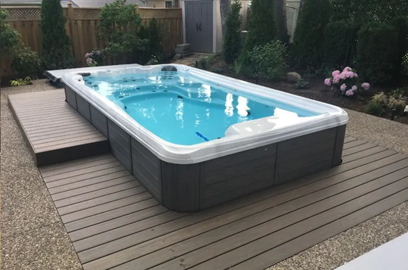 Modern above-ground pool with white rim and gray exterior on composite decking in backyard