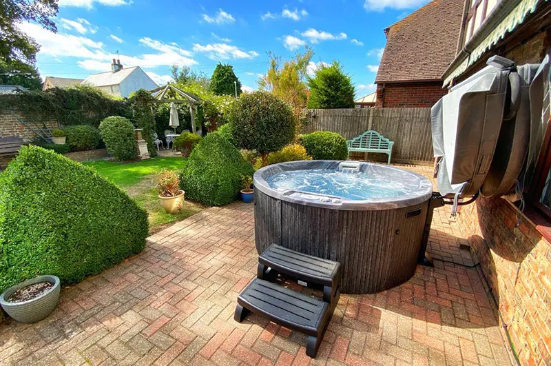 Backyard hot tub spa with wooden exterior on brick patio beside residential home